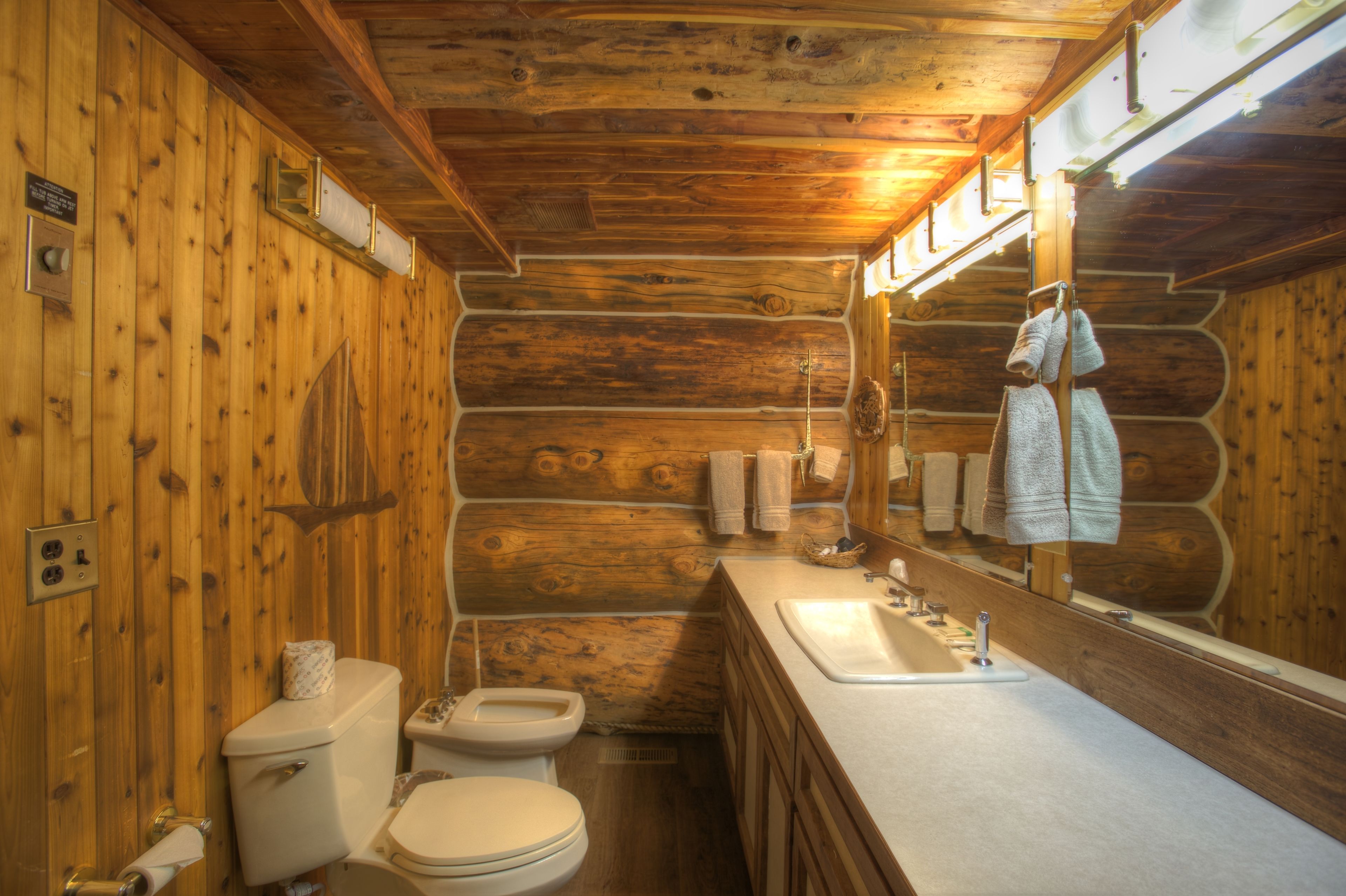 A wooden cabin-style bathroom with a toilet, sink, and mirror.