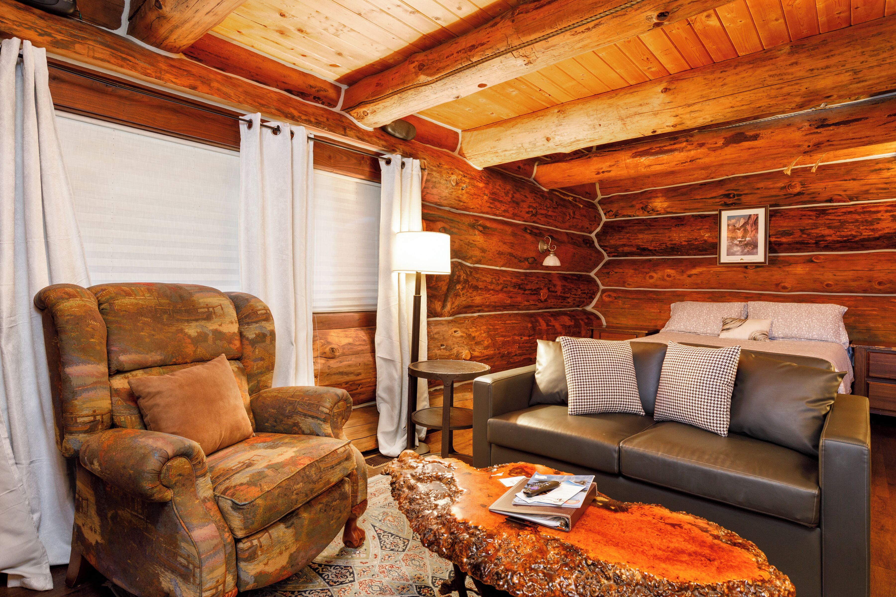 A log cabin interior with a leather armchair, a sofa, a coffee table, and a lamp.