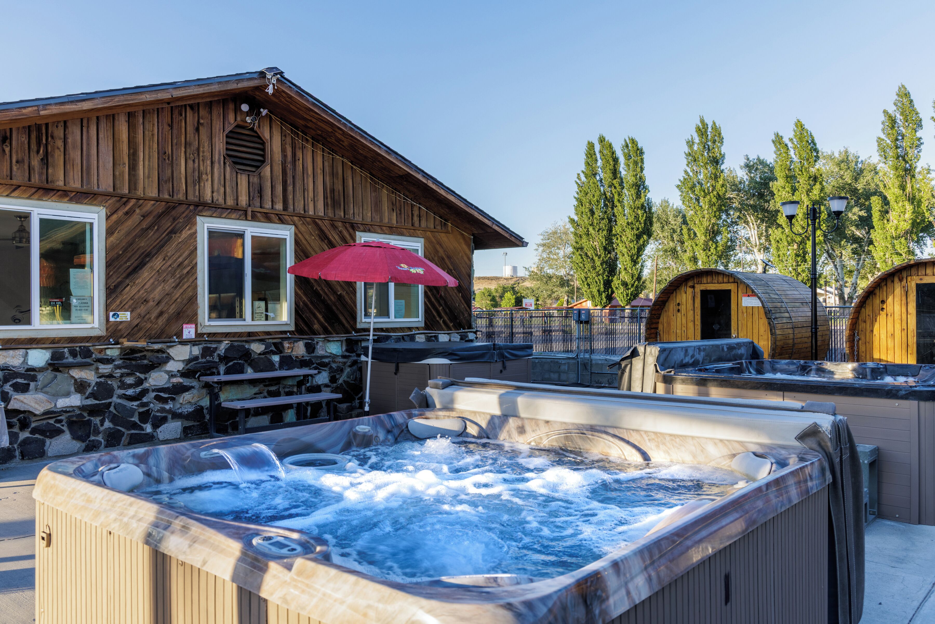 A wooden building with a stone wall, a hot tub, and two wooden cabins.