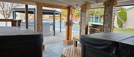 Un espace extérieur aménagé en terrasse, avec deux bains à remous, un coin salon couvert et une vue sur la rue.