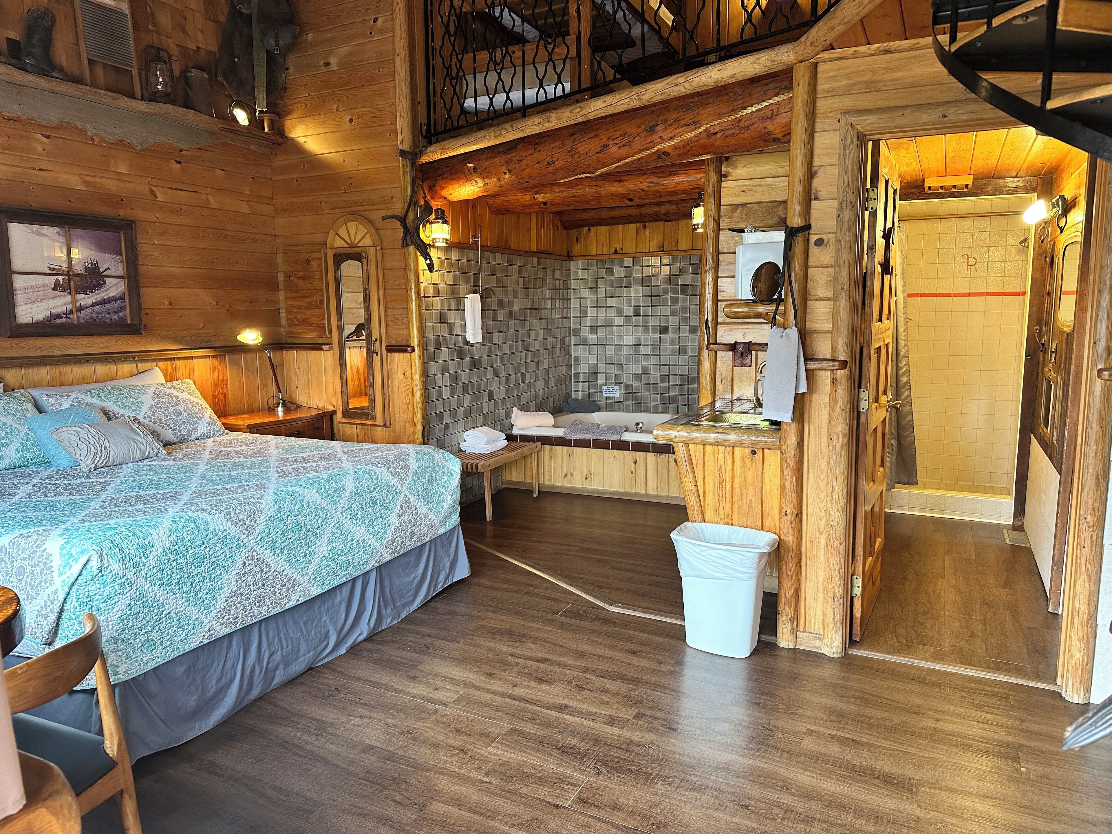 Habitación de cabaña de madera con cama, banca, pequeña mesa, ducha y escalera de madera.