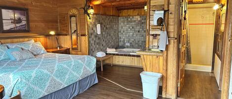 Habitación de cabaña de madera con cama, banca, pequeña mesa, ducha y escalera de madera.