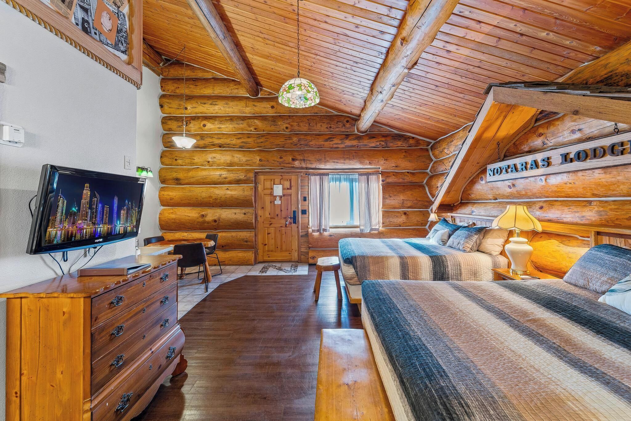 Interno di una baita di legno con televisione, mobili in legno, un letto e un cartello con la scritta 'NOTARAS LODGE'.