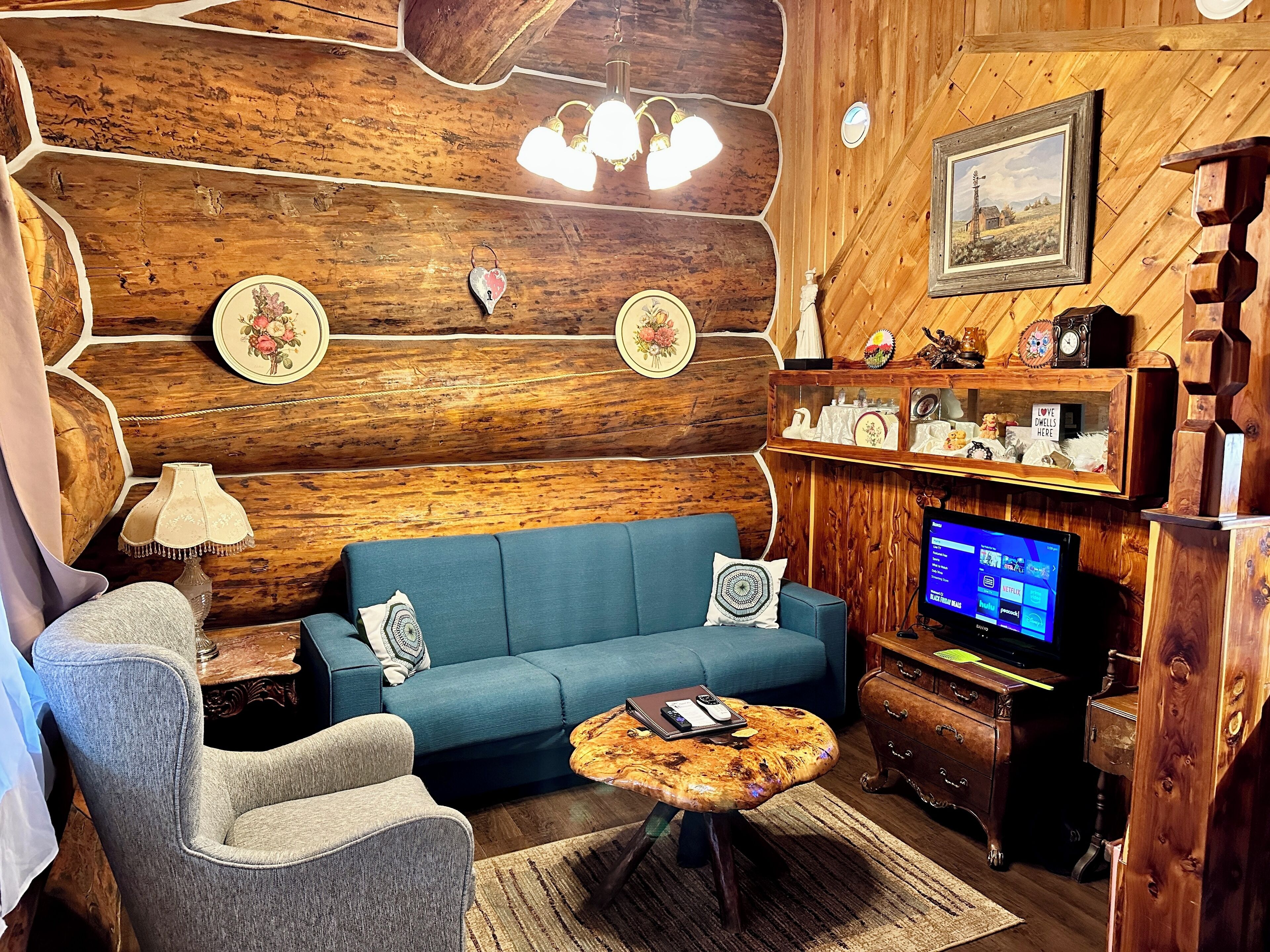 Una sala de estar acogedora con un sofá azul, un sillón gris, una mesa de centro de madera y un televisor sobre un mueble de madera.
