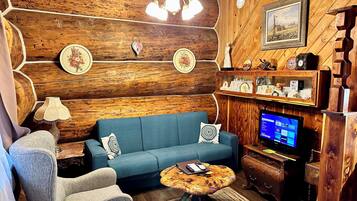 Una sala de estar acogedora con un sofá azul, un sillón gris, una mesa de centro de madera y un televisor sobre un mueble de madera.