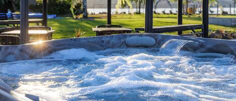 A hot tub with water jets, surrounded by outdoor seating and a view of a lake and mountains.