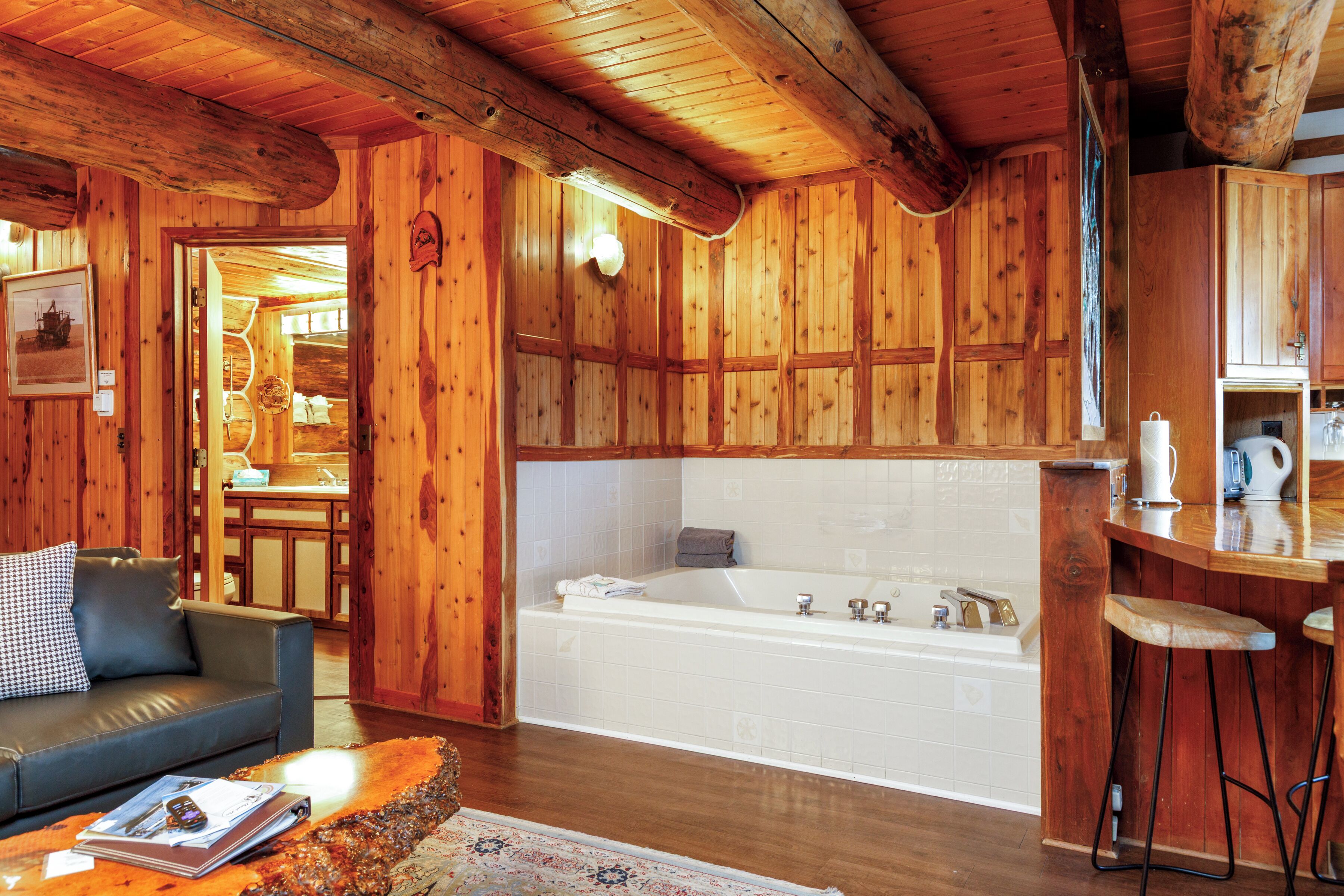 Interior de una cabaña de madera con sala de estar, una bañera grande y una zona de bar.