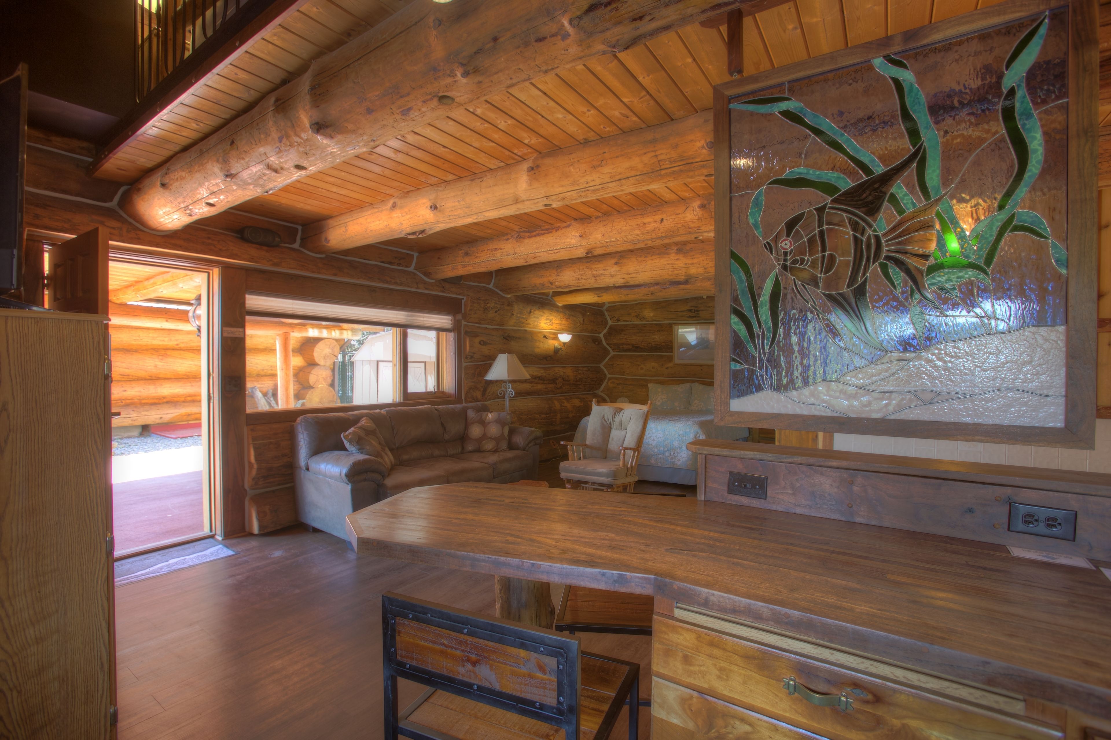 A log cabin interior with a wooden ceiling, a large fish mural, a wooden dining table, and a cozy seating area.