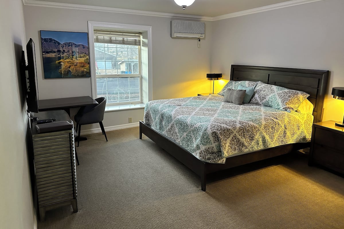 Ein Schlafzimmer mit Bett, Schreibtisch, Stuhl, Fenster und Deckenventilator.