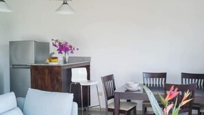 Un salon moderne comprenant un canapé, une table à manger, des chaises et un coin cuisine avec un réfrigérateur et des fleurs.