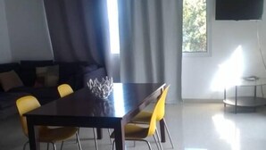 Un coin repas comprenant une table et des chaises, un canapé, un téléviseur et une fenêtre avec des rideaux.