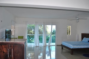 A bedroom with a bed, a desk, and a chair. There are large windows with curtains. - The Vue Apartment Hotel (Cap-Haitien)