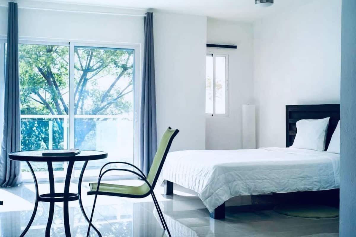 Une chambre d’hôtel avec un lit, une chaise, une table et une fenêtre donnant sur des arbres.