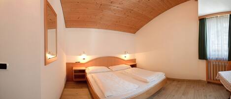 A bedroom with a curved wooden ceiling, a double bed, bedside lamps, and a window with curtains.