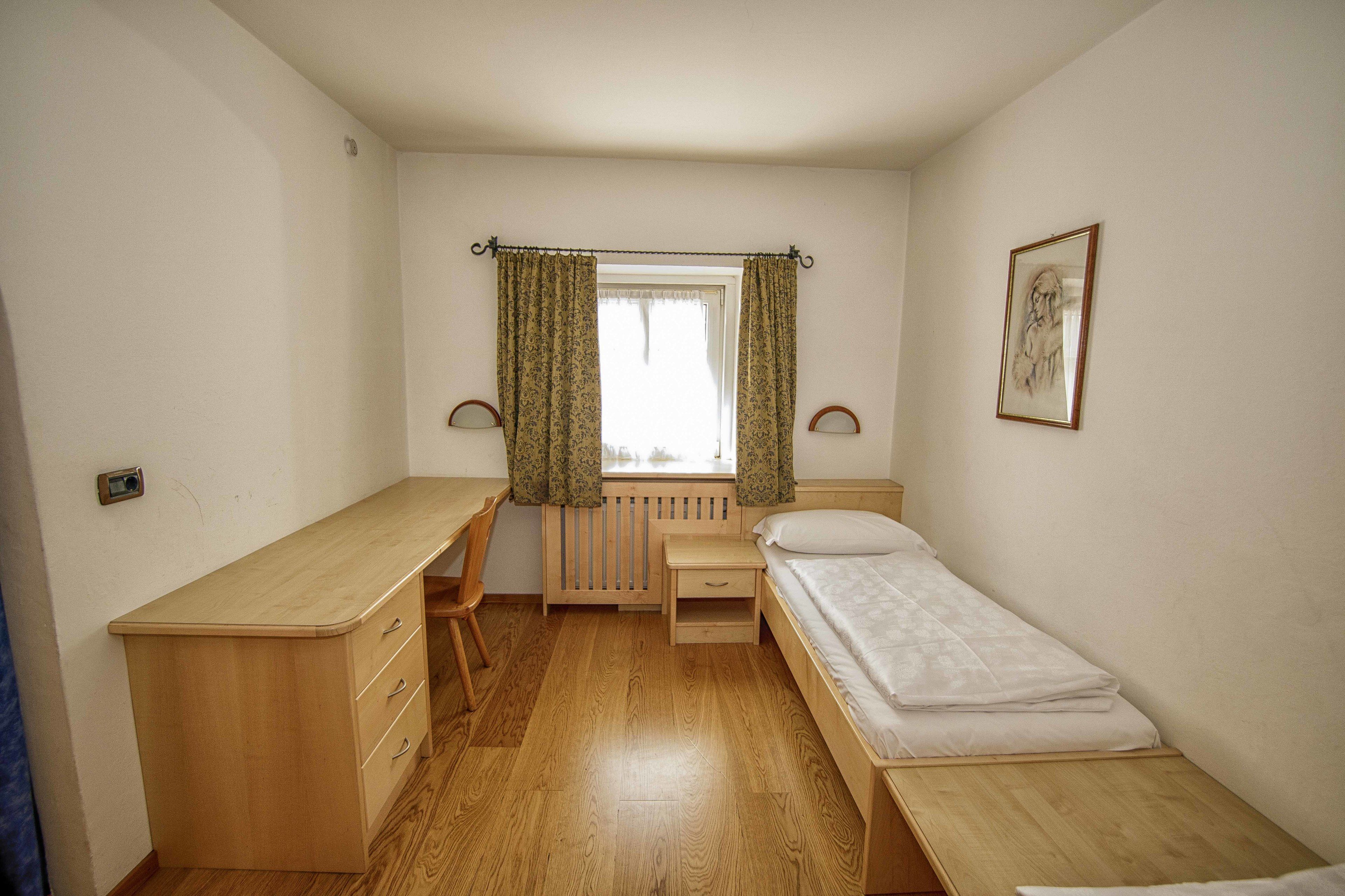 Une petite pièce, bien rangée, avec un bureau en bois, un lit simple, une chaise et un radiateur.