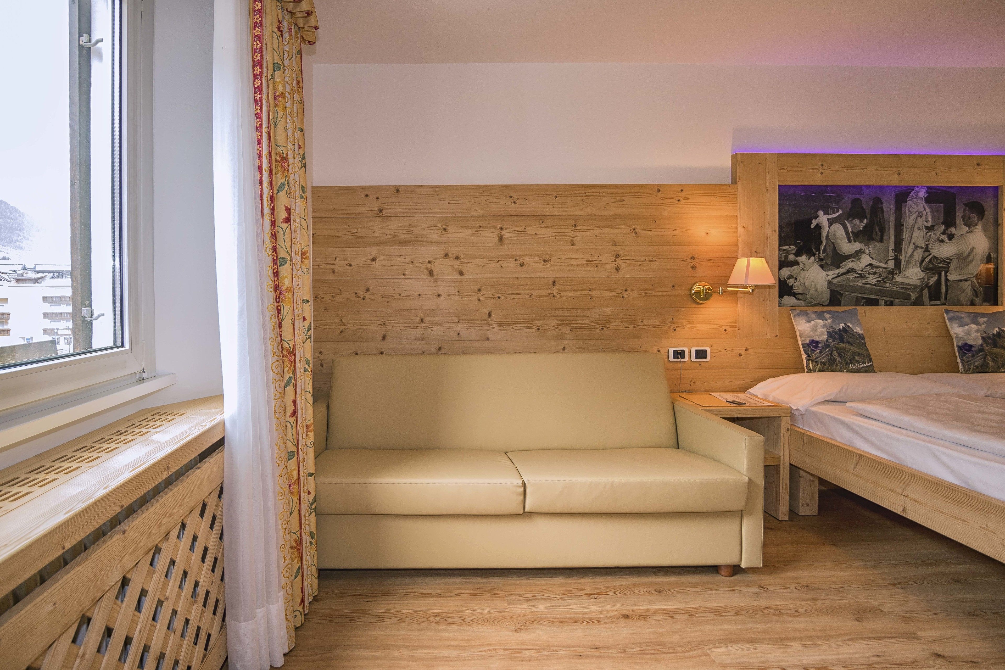 Ein Hotelzimmer mit einem Holzkopfteil, einem beigen Sofa, einem Bett mit Holzrahmen und einem an der Wand hängenden Gemälde.