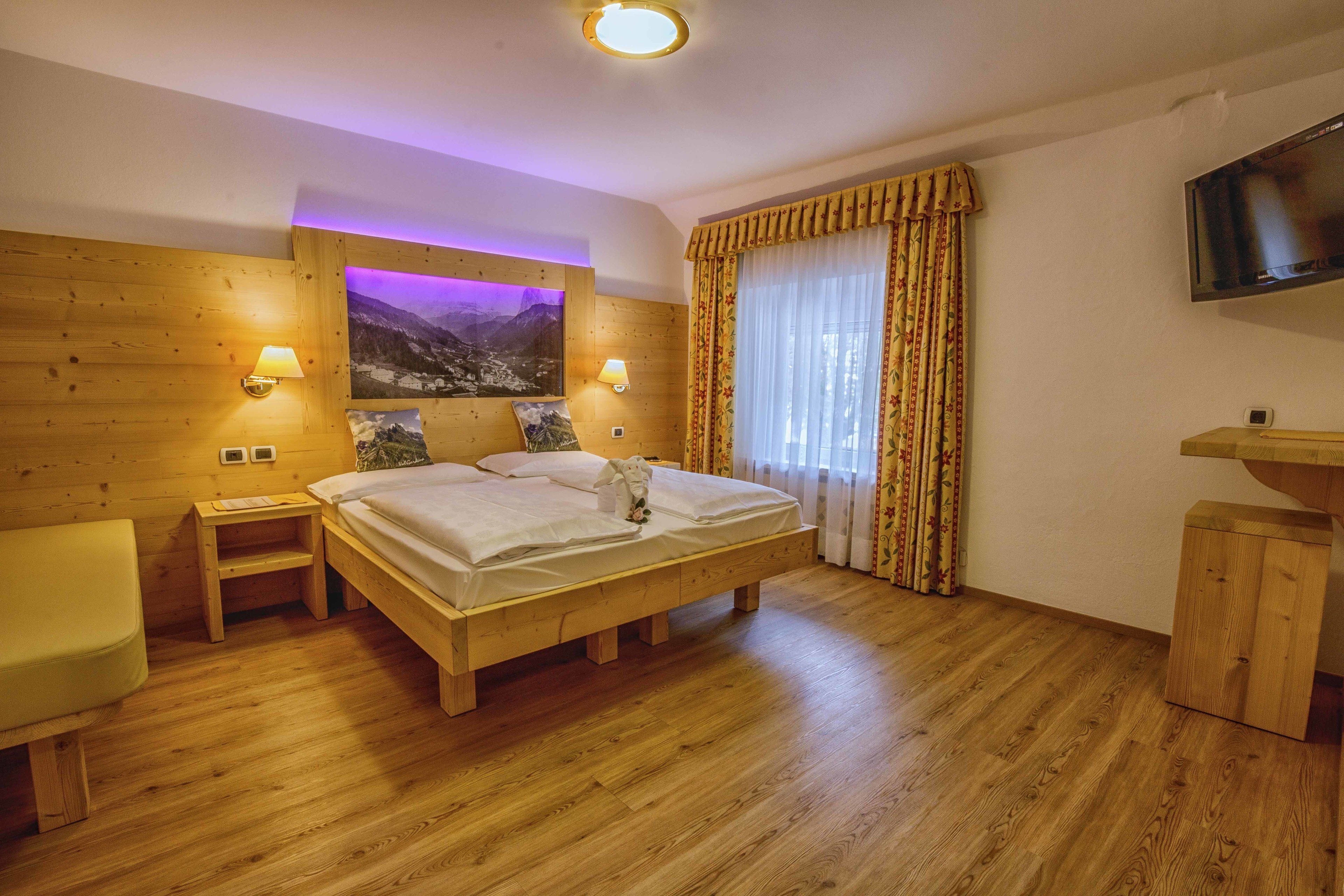 Una cama con estructura de madera y vista a la montaña, dos lámparas de noche, un televisor de pantalla plana y una mesita de noche de madera.
