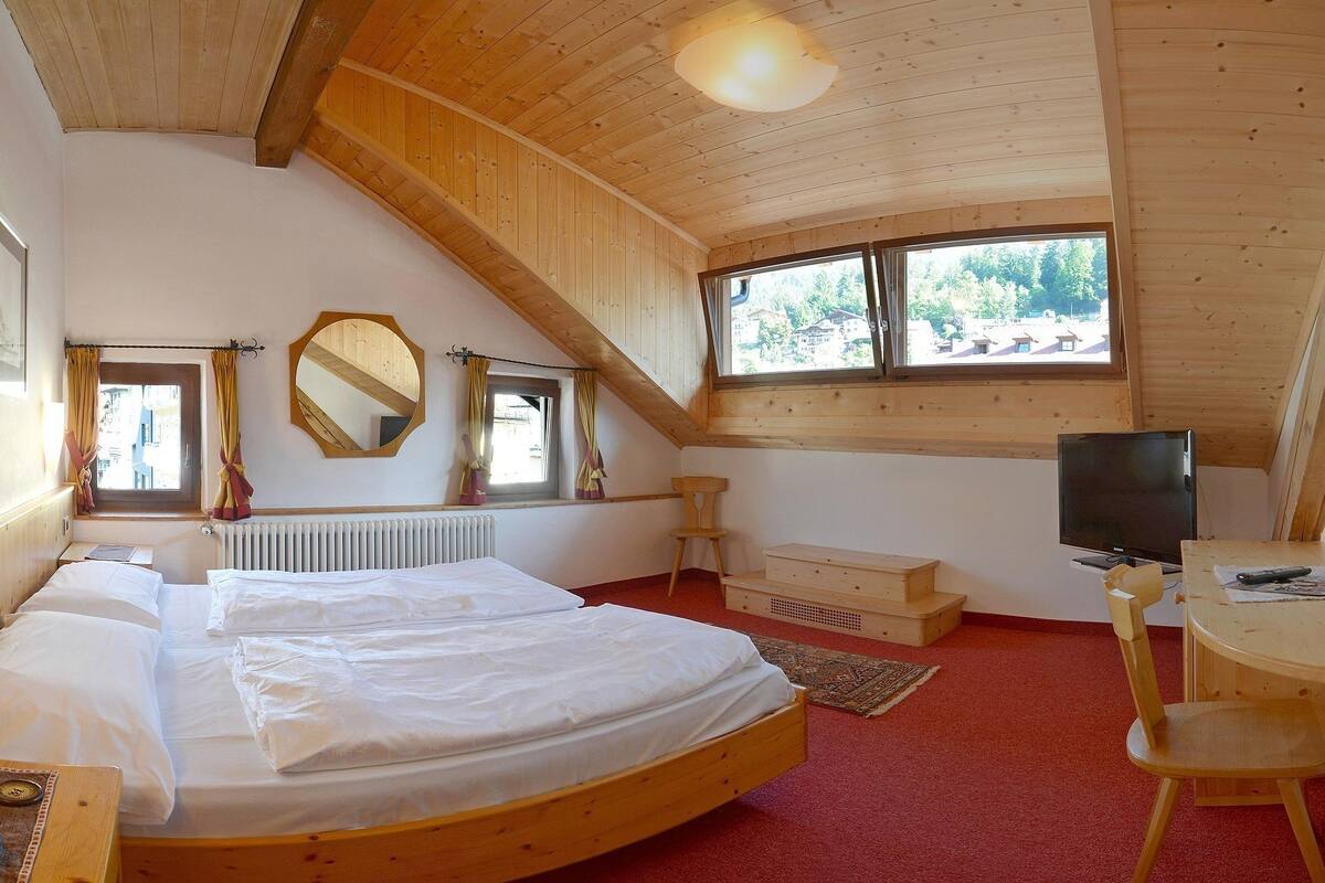 Ein Schlafzimmer mit zwei Betten, einem Fernseher, einem Schreibtisch und einem Fenster mit Blick auf Bäume.