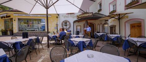 An outdoor dining area with tables and chairs, a large umbrella, and a building with a sign that reads "Ristorante."