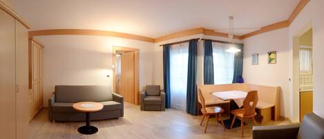 A compact living space with a sofa, a small round table, a dining table with chairs, and a kitchenette area.