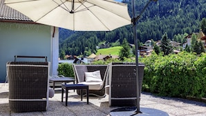 An outdoor seating area with wicker furniture and a large umbrella, overlooking a mountainous landscape.