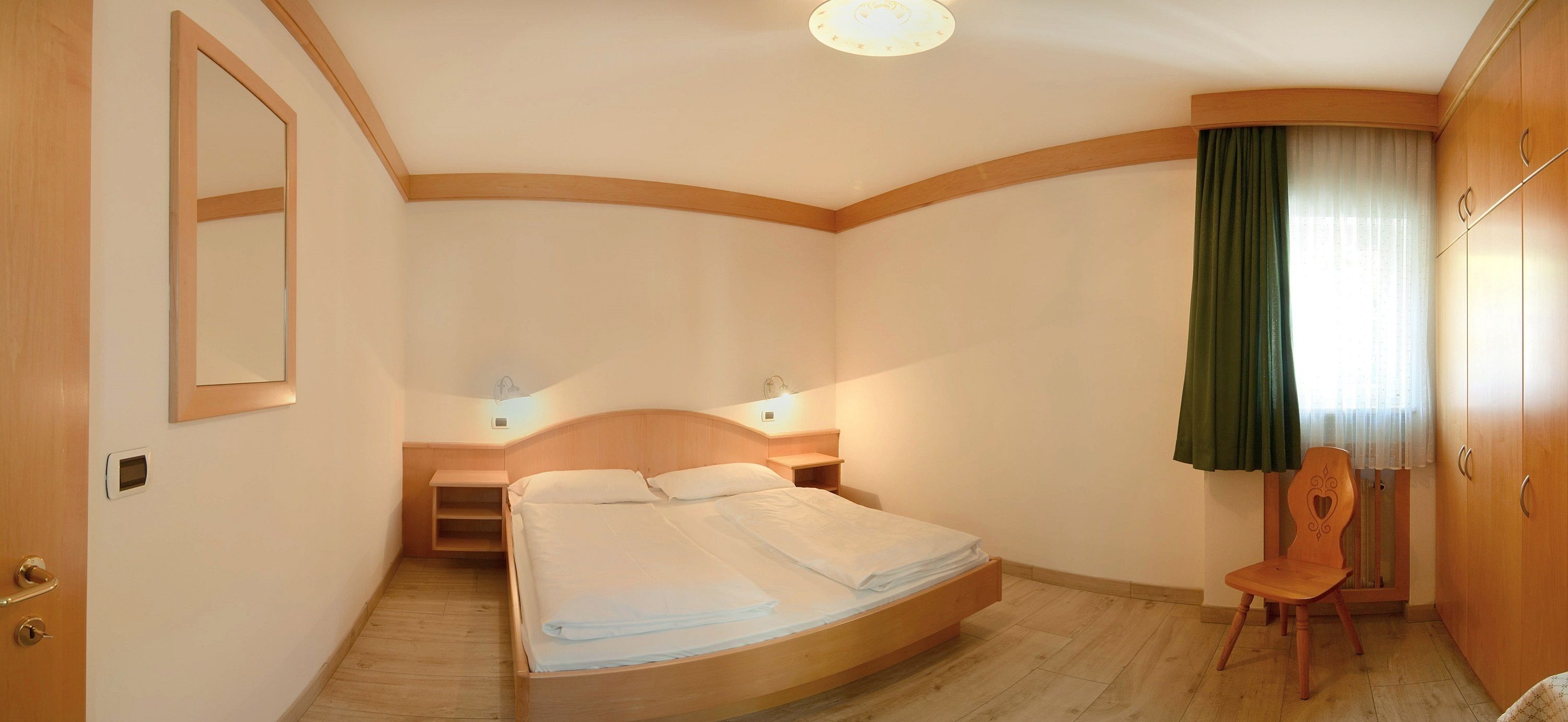 A hotel room with a bed, bedside tables, a chair, a wardrobe, and a mirror.
