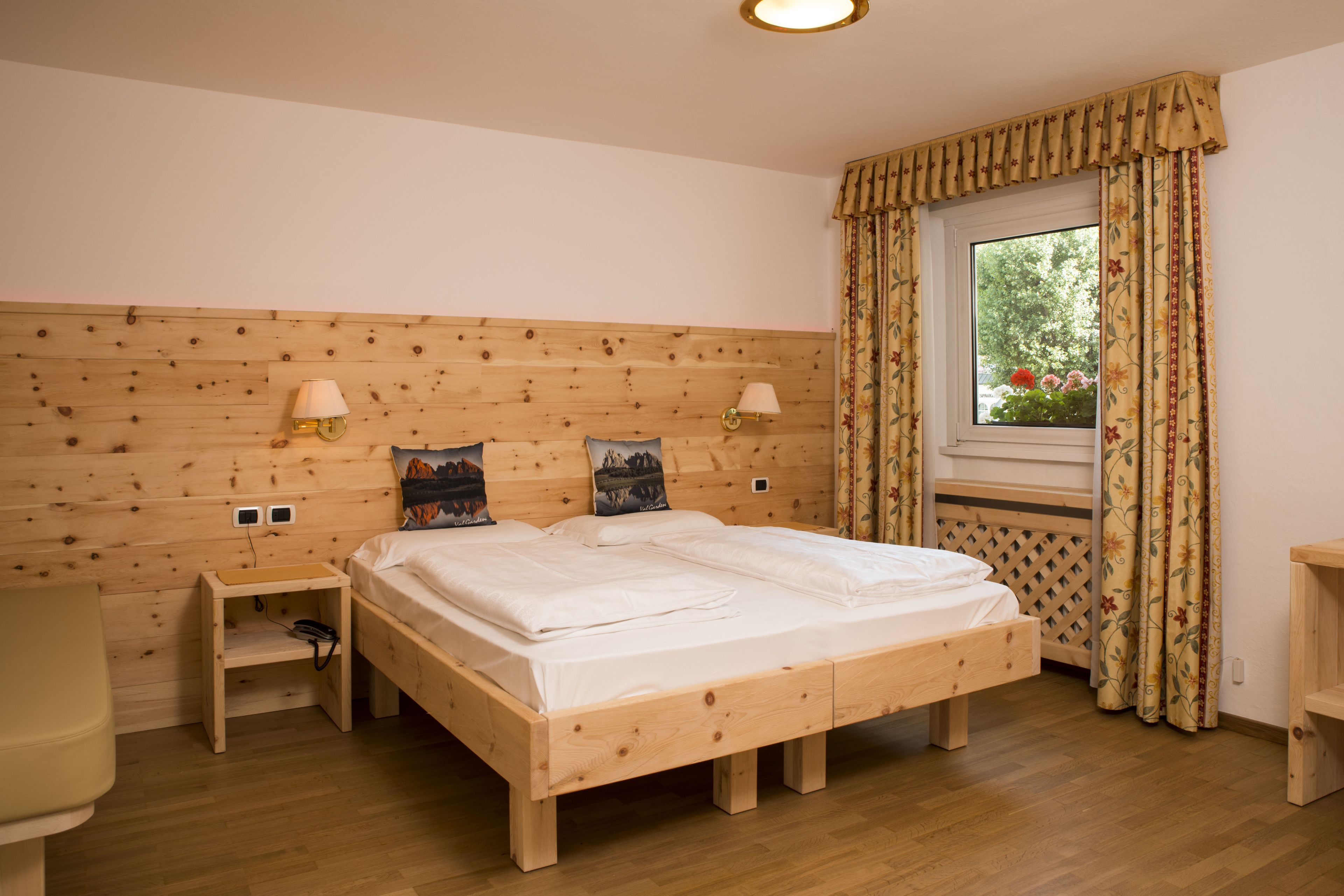 Una cama de madera con dos mesitas de noche, una ventana con cortinas y una lámpara de pared.