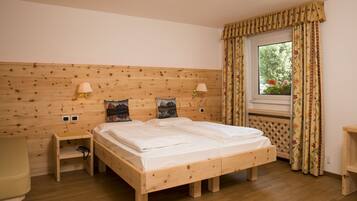 A wooden bed with two bedside tables, a window with curtains, and a wall-mounted lamp.