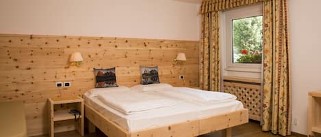 Una cama de madera con dos mesitas de noche, una ventana con cortinas y una lámpara de pared.