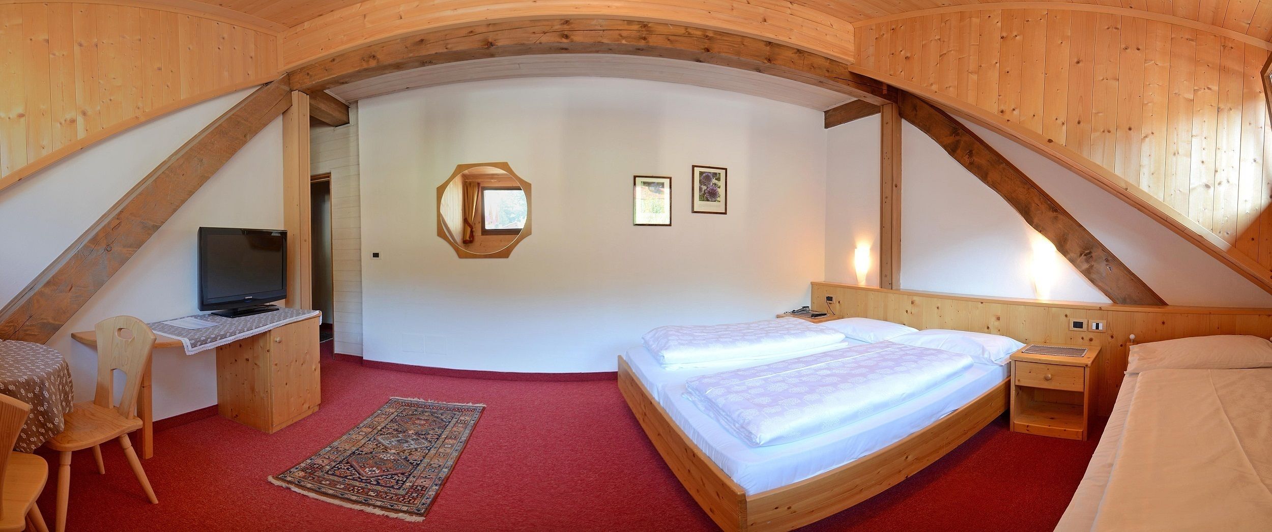 Une chambre mansardée chaleureuse avec un plafond en bois, un lit, un bureau avec une télévision et un petit tapis.