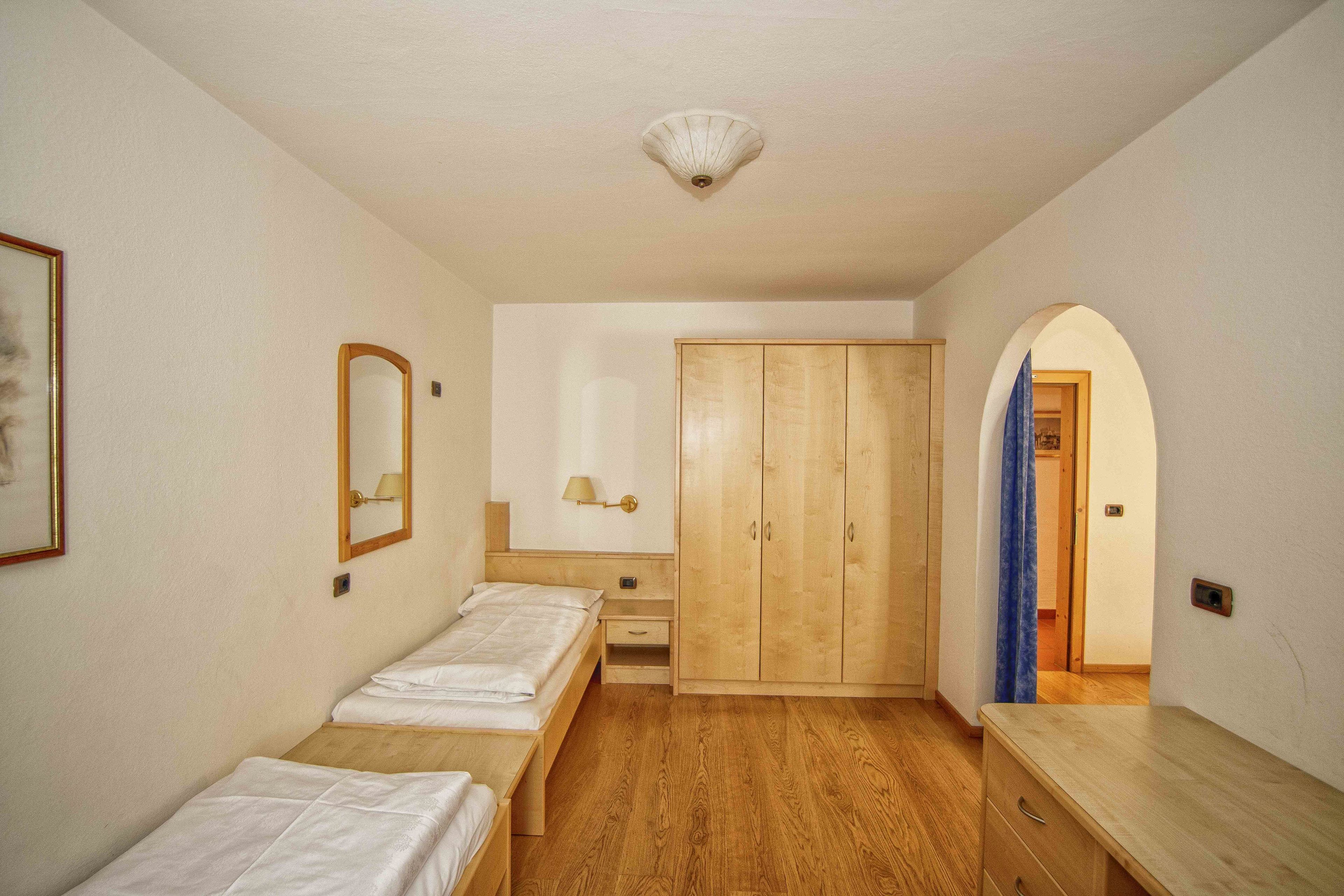 Quarto com duas camas de solteiro, guarda-roupa de madeira, mesa de cabeceira com abajur e espelho na parede.