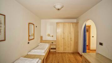 Quarto com duas camas de solteiro, guarda-roupa de madeira, mesa de cabeceira com abajur e espelho na parede.