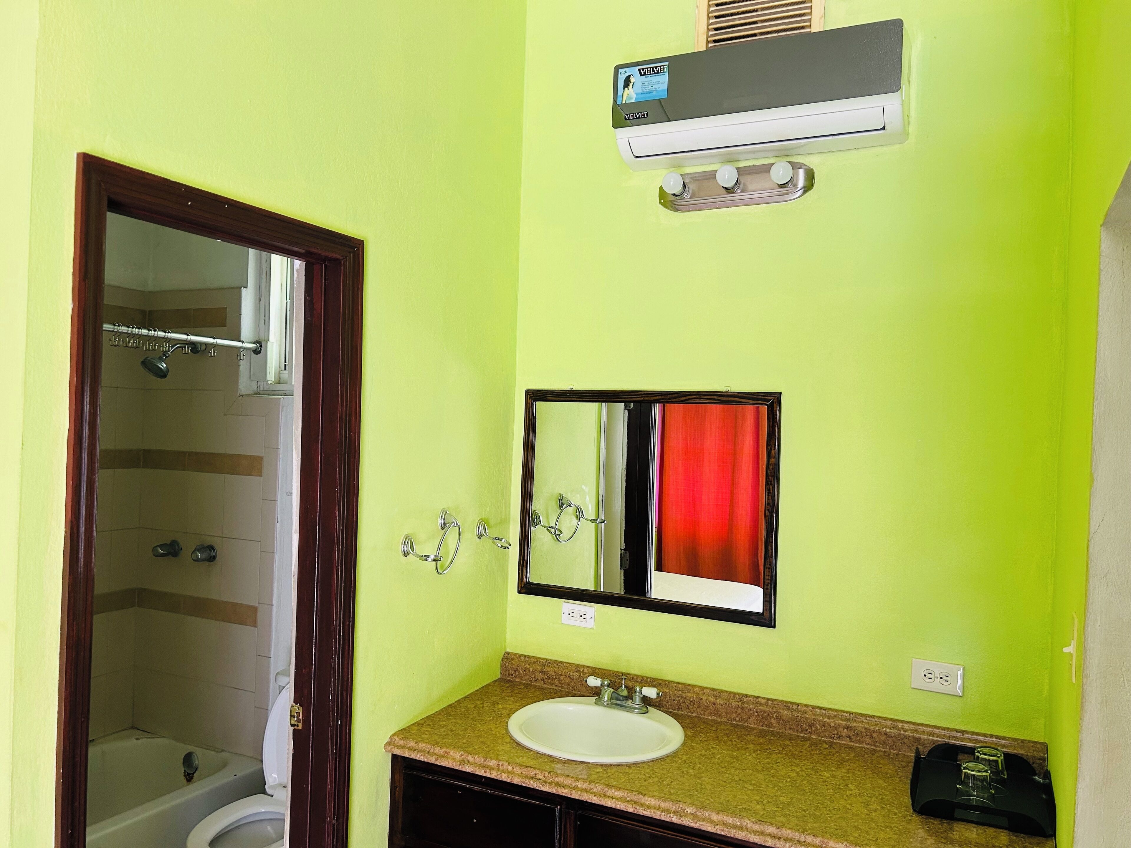 A bathroom with a green wall, a white sink, a mirror, and a shower area.