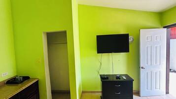 A room with a green wall, a white door, a black TV mounted on the wall, a black filing cabinet, and a wooden cabinet with a countertop.