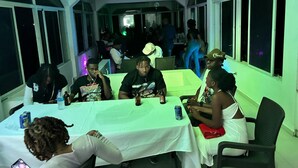 A group of people seated at a table with a white tablecloth, in a room with large windows and a high ceiling. - Arawak Hotel (Léogâne)