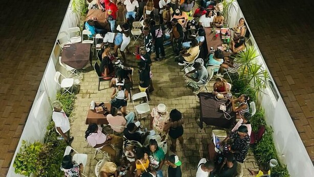 An outdoor seating area with tables and chairs arranged around a central stage, surrounded by a low wall and potted plants. - Arawak Hotel (Léogâne)