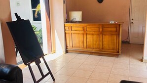 A room with a wooden cabinet, a ceiling fan, a painting on the wall, and a door. - Arawak Hotel (Léogâne)