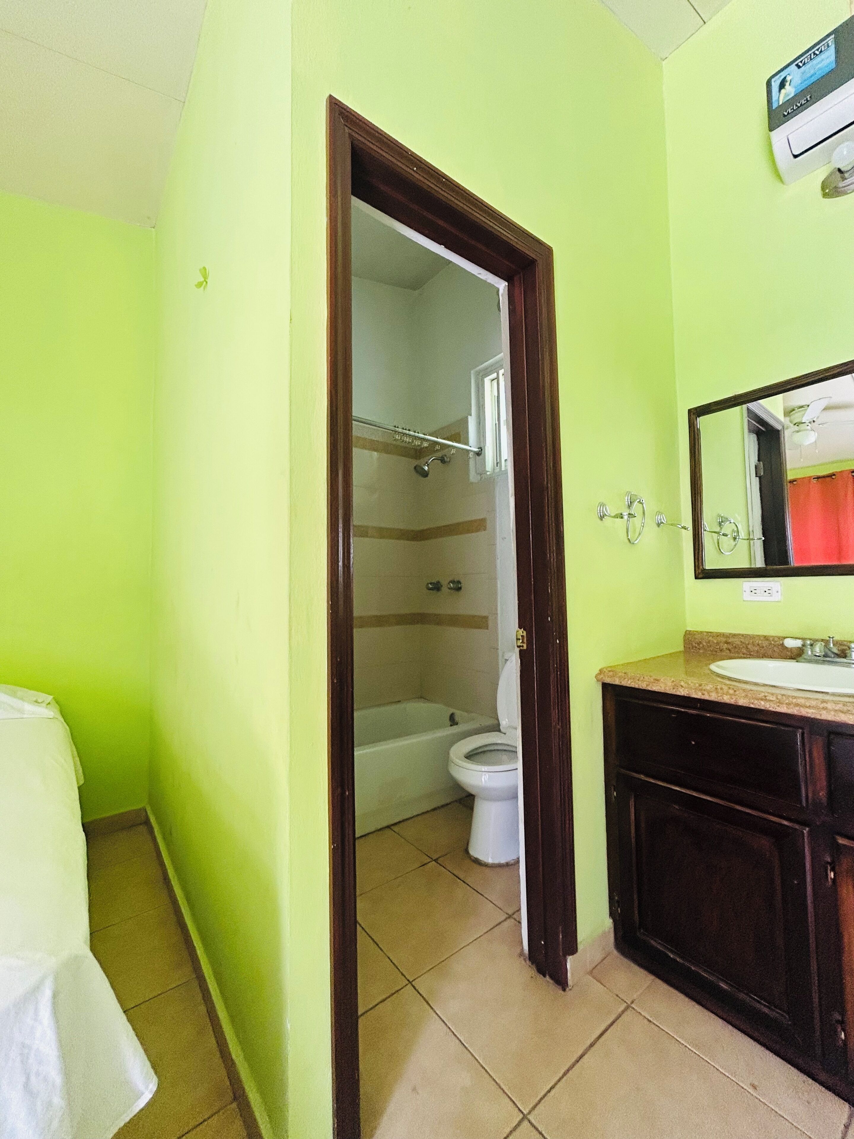 Un baño con pared verde, inodoro blanco, bañera y tocador con espejo.