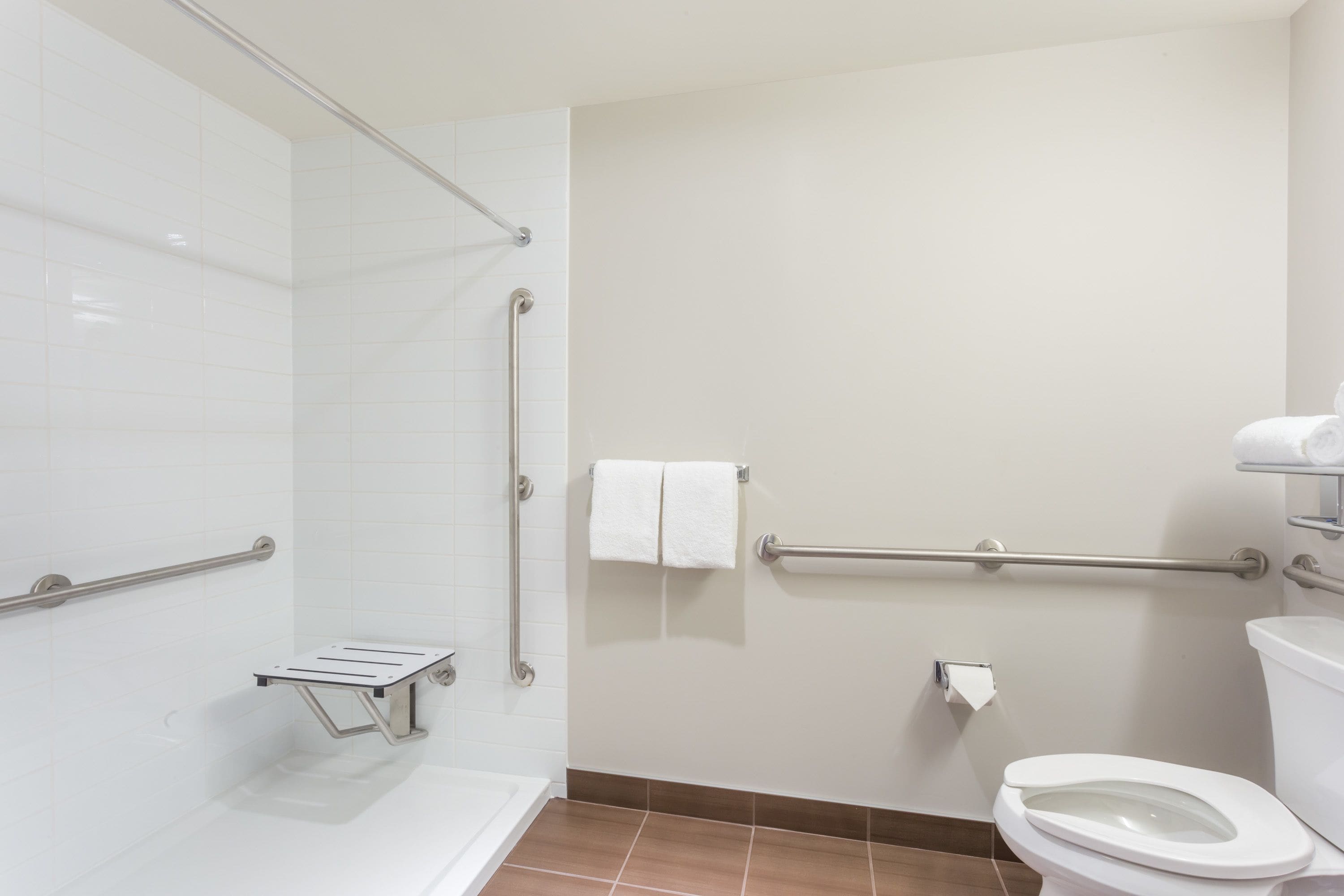 Un baño con inodoro blanco, pasamanos, barra de apoyo, toallero y dispensador de toallas de papel.