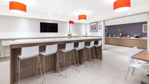 A modern kitchen with a long island, white bar stools, and red pendant lights. - Microtel Inn & Suites By Wyndham Fort Mcmurray (Fort McMurray)
