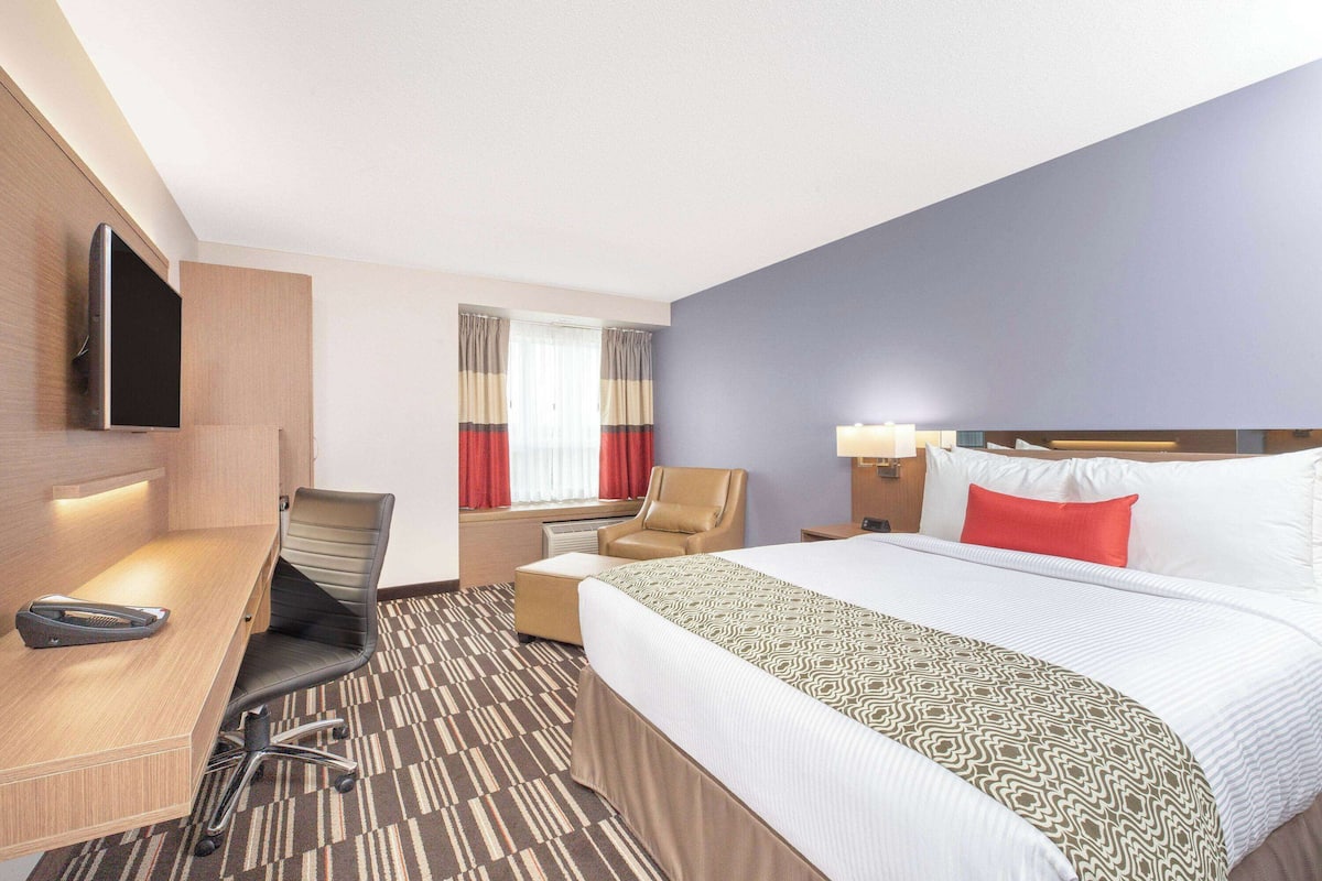 Ein Hotelzimmer mit Bett, Schreibtisch, Sessel, Fernseher und einem Fenster mit Vorhängen.