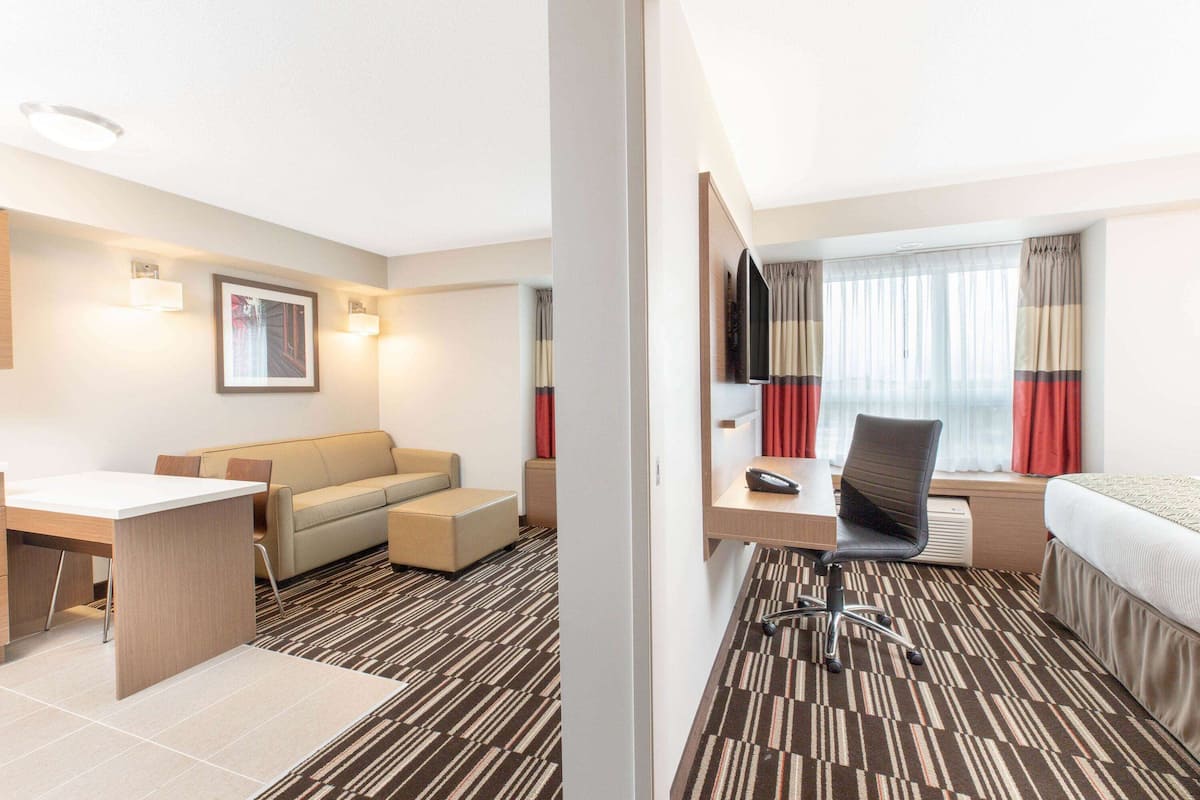 Ein Hotelzimmer mit Bett, Schreibtisch, Sessel, Sofa, Fernseher und einem Fenster mit Vorhängen.