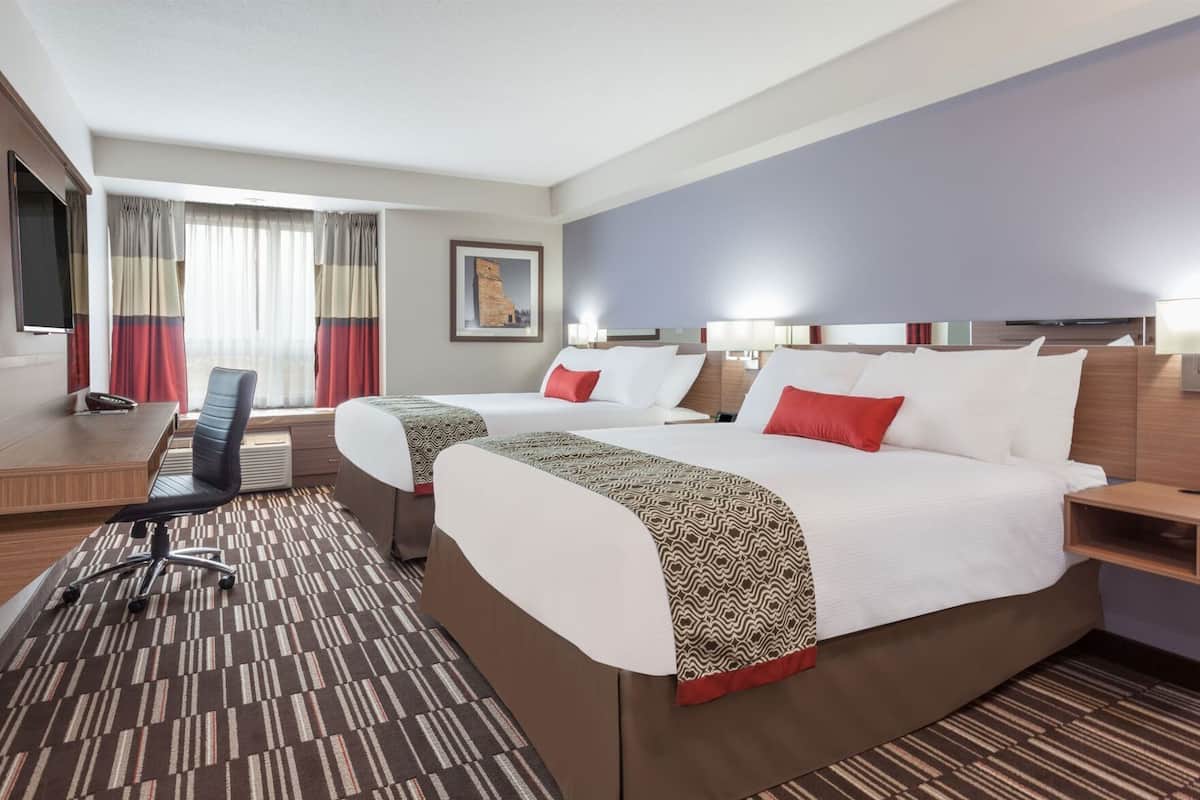 Ein Hotelzimmer mit zwei Betten, einem Schreibtisch, einem Stuhl und einem großen Fenster mit Vorhängen.