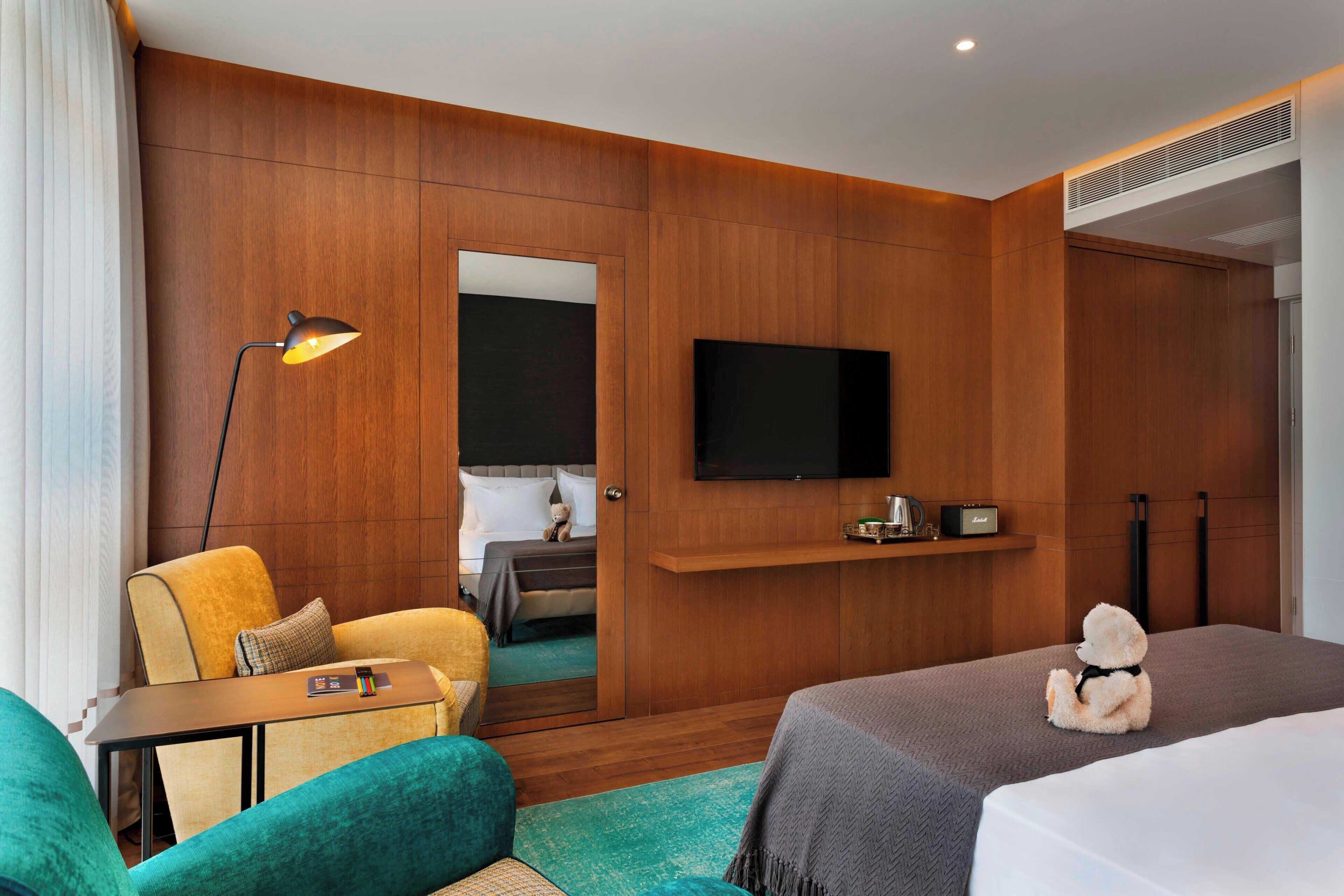 Habitación de hotel con pared de madera, televisor de pantalla plana, cama, sofá, escritorio y un oso de peluche.