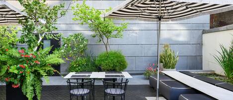 An outdoor patio with a table and chairs, a striped umbrella, and various plants.