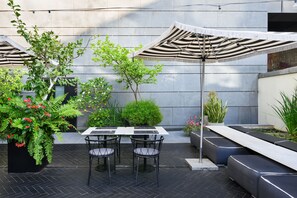 Un patio al aire libre con una mesa, sillas, un paraguas a rayas y diversas plantas.