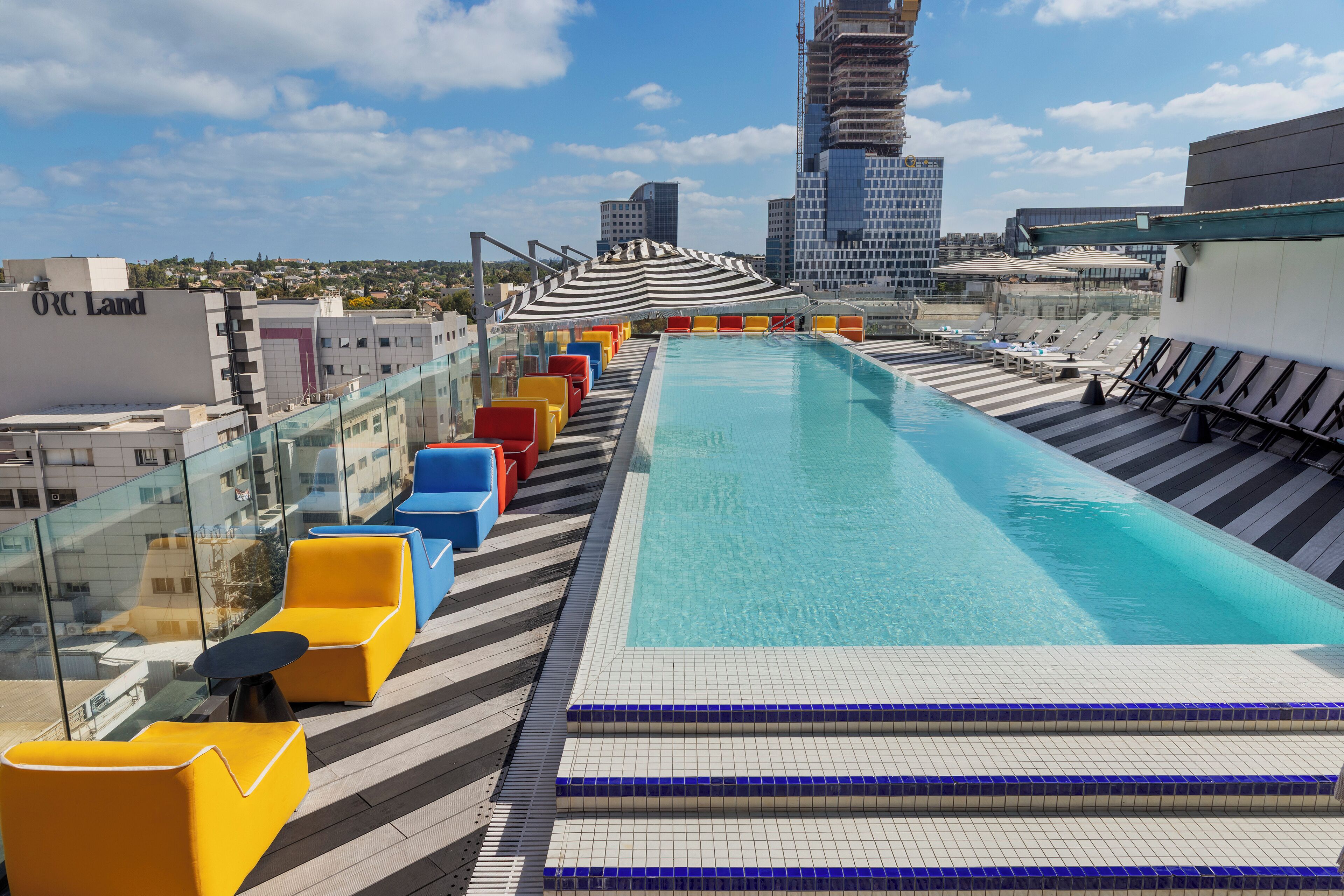 A rooftop swimming pool with a clear view of the city skyline, including a tall building under construction.