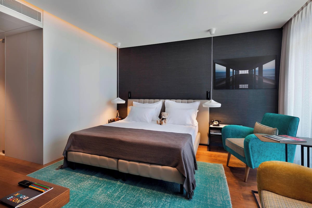 A modern hotel room with a large bed, a small desk, a chair, and a view of a bridge.
