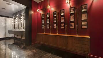 A reception area with a wooden counter, framed pictures on the wall, and a mirror with lights above it.
