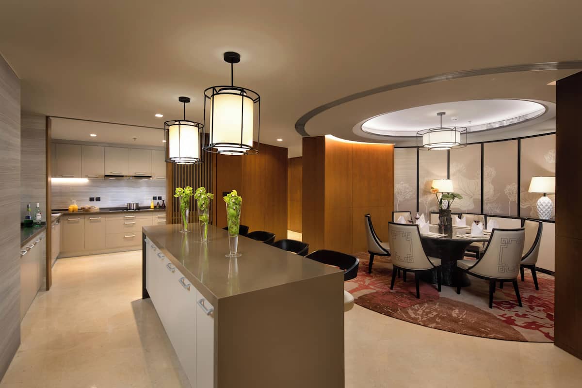 Una cocina moderna con una isla central, comedor con mesa redonda y sillas, e iluminación colgante.